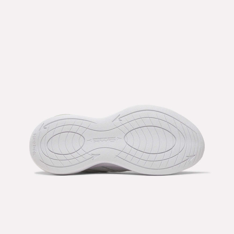The image displays the white rubber outsole of the Reebok Women’s DMX Comfort + Walk Ultra Shoes, featuring curved grooves and textured patterns for improved grip, as seen from the bottom against a plain light background. This outsole design works together with DMX Comfort+ cushioning to deliver enhanced comfort and support during every step.
