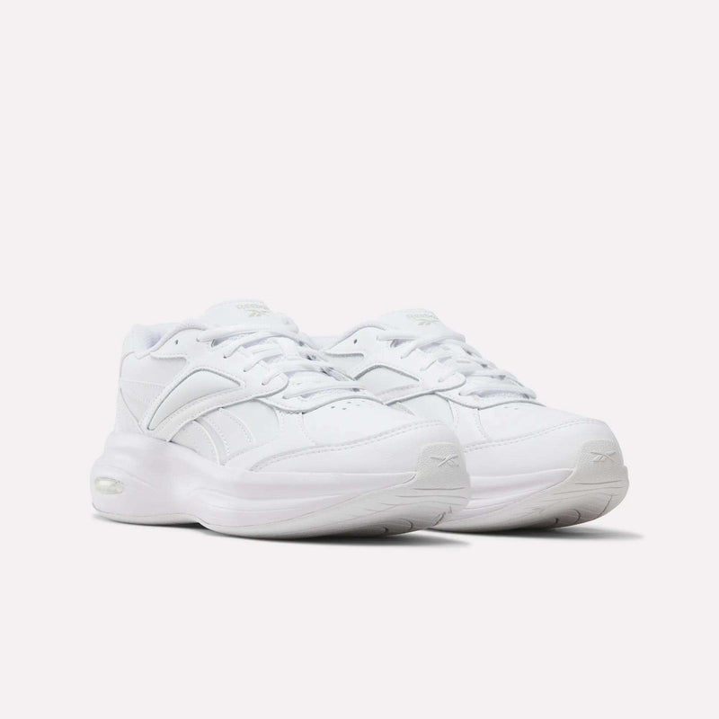 A pair of white Reebok Women’s DMX Comfort + Walk Ultra Shoes, featuring laces, thick soles, minimal branding, and DMX Comfort+ cushioning, are positioned side by side on a plain white background.