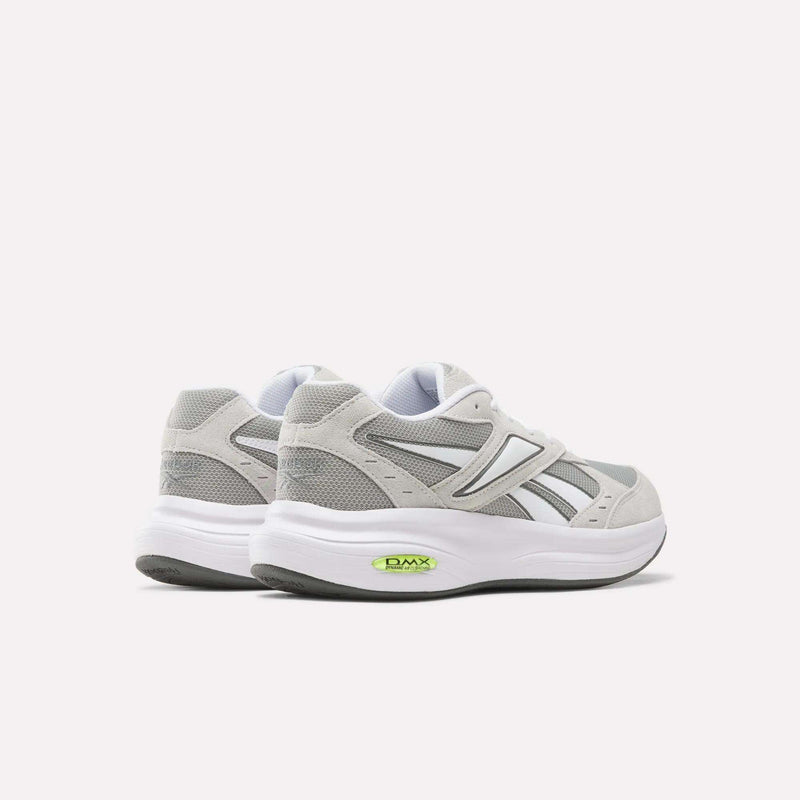 A pair of Reebok Men’s DMX Comfort+ Walk Ultra Shoes in gray and white, featuring green DMX Comfort+ cushioning visible in the soles, are displayed on a light background and angled to highlight the backs and sides of these athletic walking sneakers.