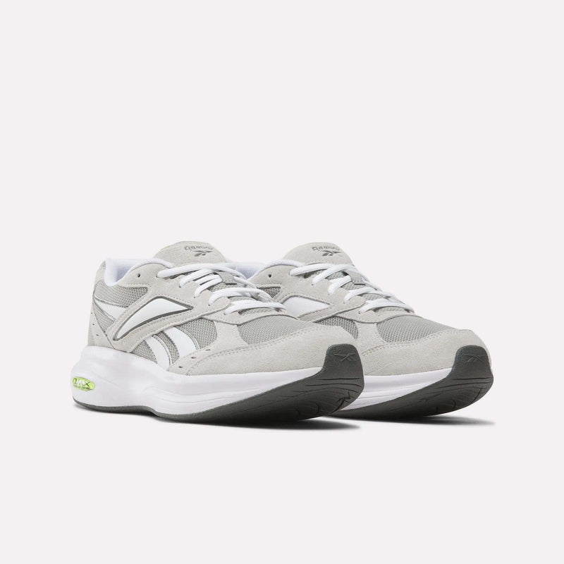A pair of Reebok Men’s DMX Comfort+ Walk Ultra Shoes in light gray and white, featuring white laces, a chunky white sole with black accents on the outsole, and a small green detail near the heel. These athletic sneakers are designed with Reebok’s DMX Comfort+ technology for superior cushioning, and are displayed on a plain white background.