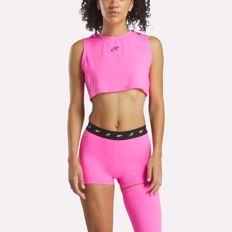 A woman wears the Reebok x Angel Reese Crop Tank Top by Reebok with matching high-waisted shorts featuring a black waistband, standing against a plain white background.
