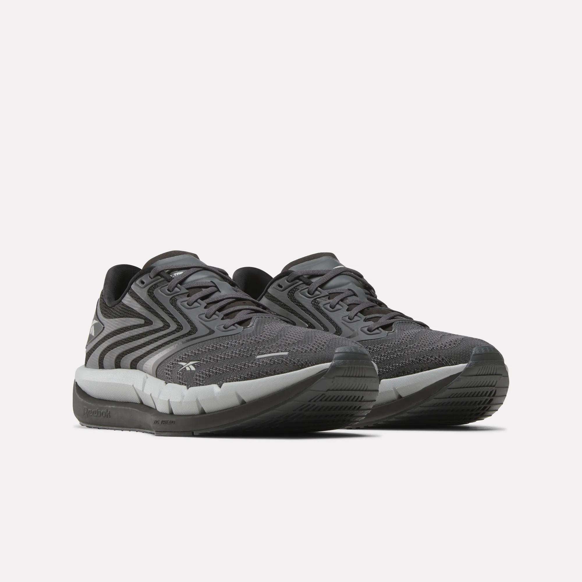 The Reebok Men's FloatZig Tread Running Shoes feature dark gray patterned mesh uppers, black laces, and a cushioned midsole—ideal for treadmill workouts—shown on a plain white background.