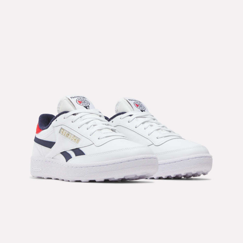 The Men's Club C Revenge Golf Shoes by Reebok are white with navy blue and red accents, feature the Reebok logo on the tongue and side, and have a spikeless outsole for traction, shown against a plain light background.