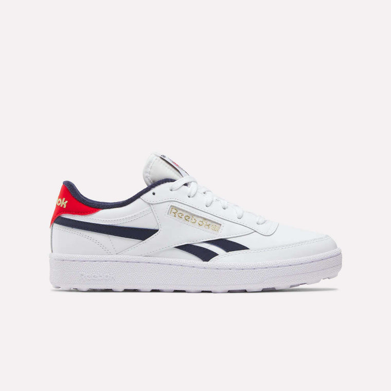 The Reebok Men's Club C Revenge Golf Shoes feature a white design with navy and red accents, gold branding, a red logo heel tab, and spikeless outsole for comfort on or off the golf course.