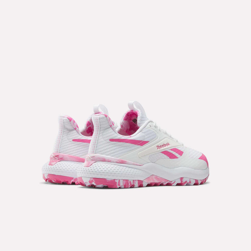A pair of Reebok Nano Golf Shoes with white uppers, pink accents, and pink camo-patterned soles, featuring a lightweight FlexWeave upper, displayed against a plain light background.