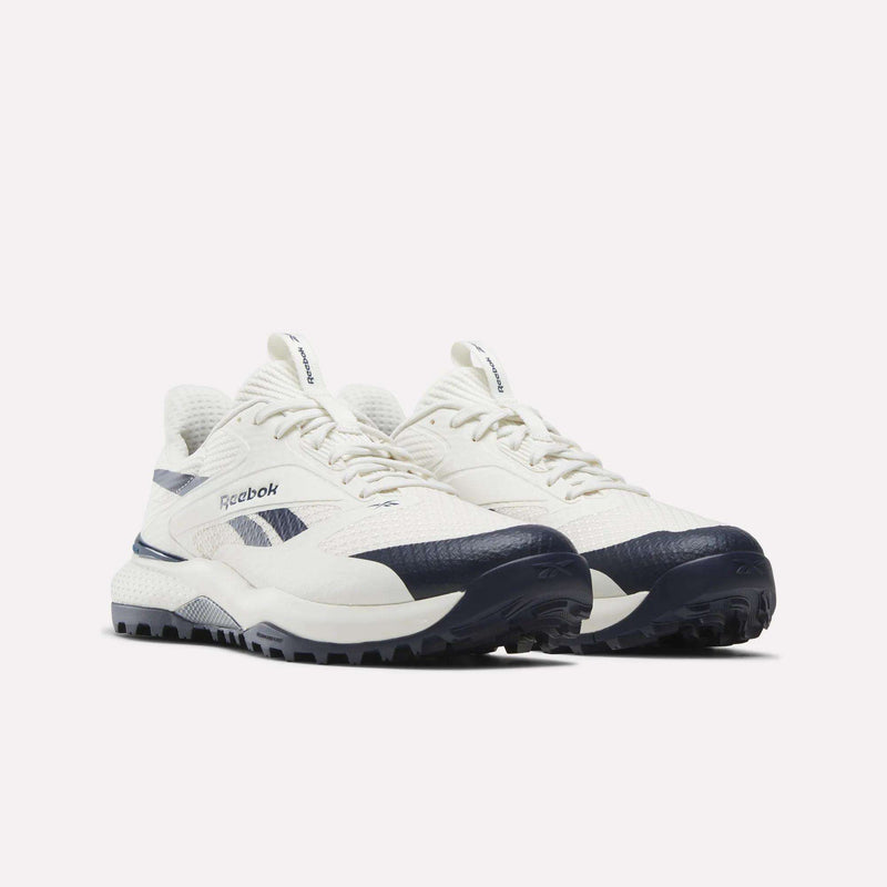 A pair of Reebok Nano Golf Shoes in white with navy blue accents and textured soles, featuring advanced Floatride foam for superior cushioning, positioned side by side on a plain light background.