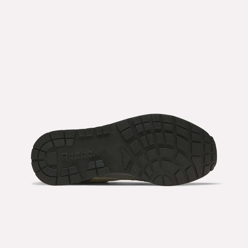 The image displays the bottom view of a black Men's GL1600 Shoe sole by Reebok, showcasing a textured tread pattern designed for enhanced grip against a white background. Inspired by Reebok's archives, these sneakers typically feature a suede upper that combines retro style with modern performance.