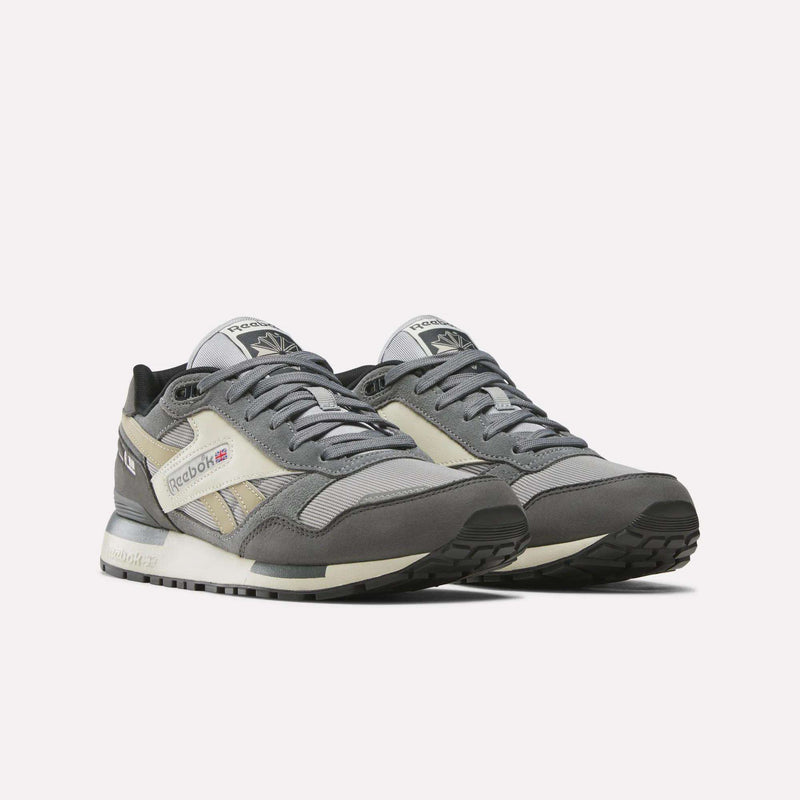 A pair of Reebok Men's GL1600 Shoes, inspired by archival designs, in shades of gray and off-white with a suede upper, black soles, and mesh details, displayed against a plain white background.