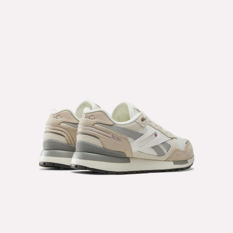 A pair of Men’s GL1600 Shoes by Reebok in beige and white suede are displayed at an angle to showcase the sides and back, featuring gray outsoles with subtle pink and tan accents, set against a plain white background.