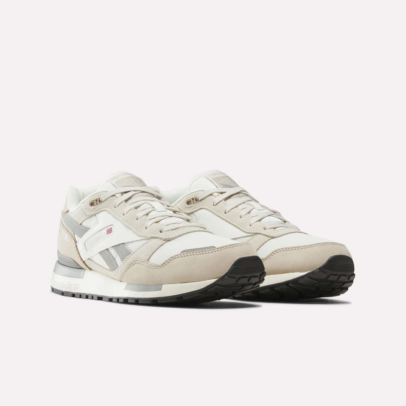 A pair of Men’s GL1600 Shoes by Reebok in beige and white with gray accents, featuring suede uppers, lace-up fronts, and durable rubber soles. These athletic sneakers are displayed side by side on a white background, offering everyday comfort and timeless style.