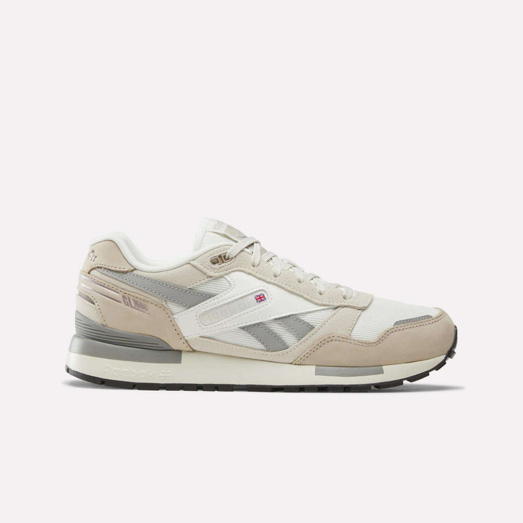 A pair of Reebok Men’s GL1600 Shoes in Elevated Beige, Linen, and Chalk is displayed on a plain white background. Featuring a low profile design inspired by the classic GL1600, these sneakers showcase side branding, a small flag detail, a durable rubber sole, and subtle suede accents for added texture and style.