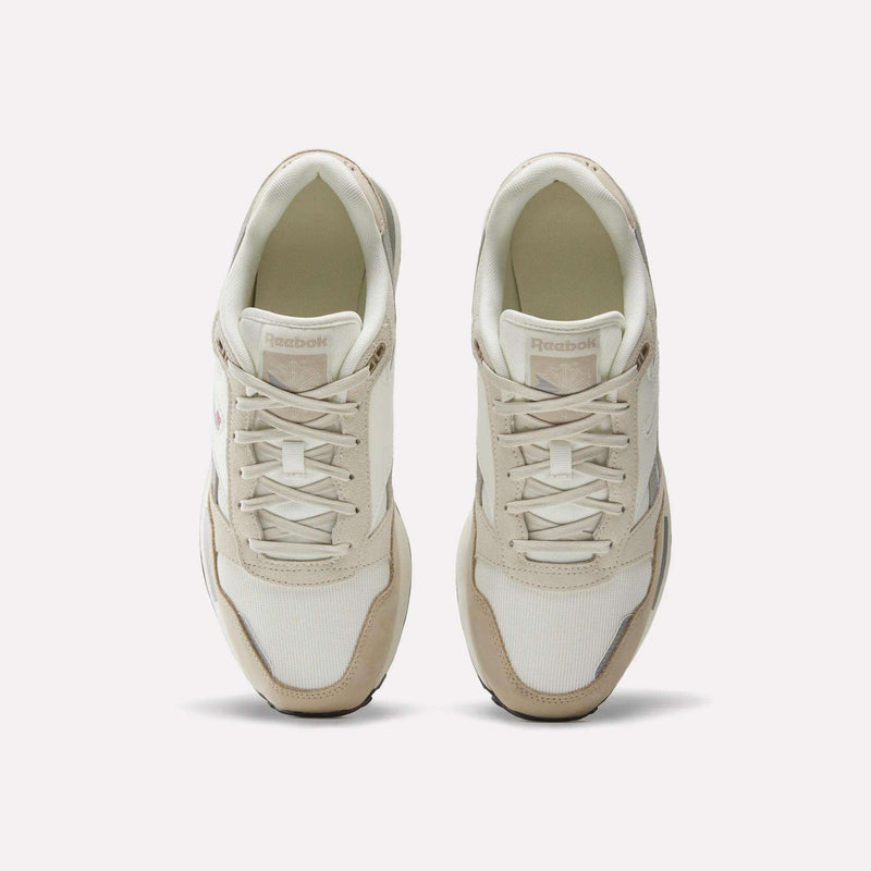 A pair of Men’s GL1600 Shoes by Reebok in cream and beige, viewed from above, showcasing the laces and the Reebok branding on the tongue of each shoe. Subtle suede accents lend a classic touch to these stylish sneakers.