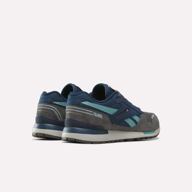 Men’s GL1600 Shoes by Reebok in a combination of navy blue, teal, and gray are displayed against a plain white background, shown from the back and side views. These heritage-inspired sneakers offer classic style and comfortable wear for everyday use.