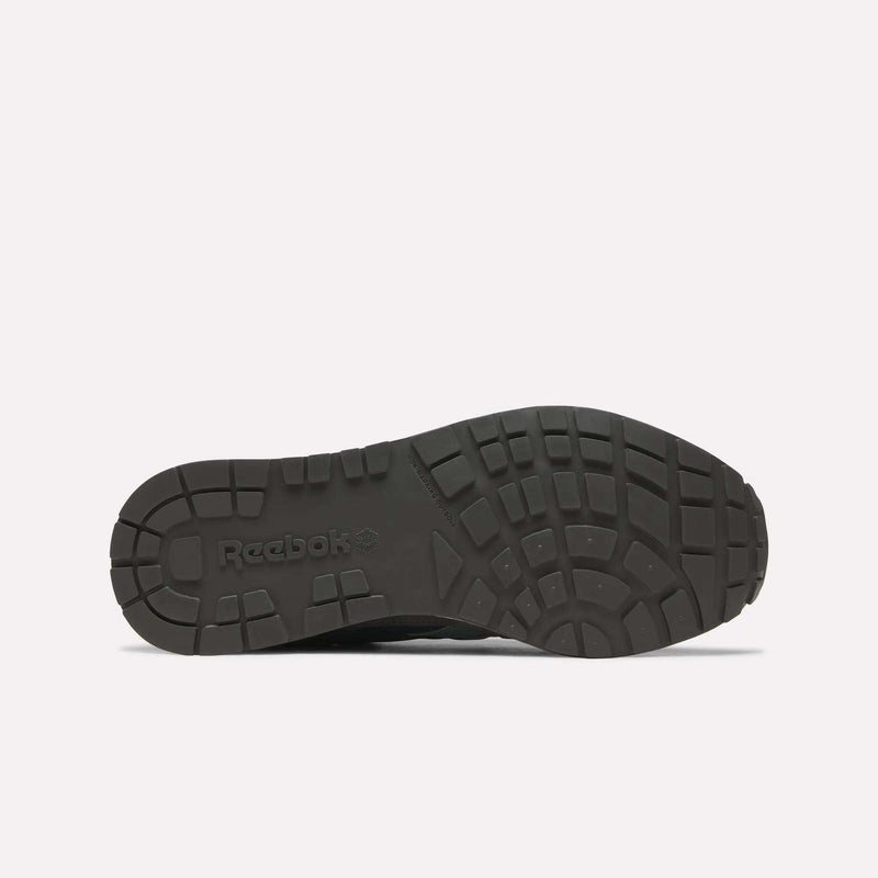 The image displays the black rubber outsole of the Reebok Men’s GL1600 Shoes, viewed from beneath, featuring a textured tread design and the Reebok branding. This detail showcases both the durability and distinctive style of these heritage-inspired sneakers.