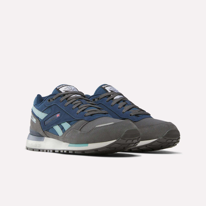 A pair of Reebok Men’s GL1600 Shoes, featuring a heritage-inspired design in blue and gray with white midsoles, teal accents, and black outsoles, displayed against a plain white background—ideal for anyone seeking stylish yet comfortable footwear.
