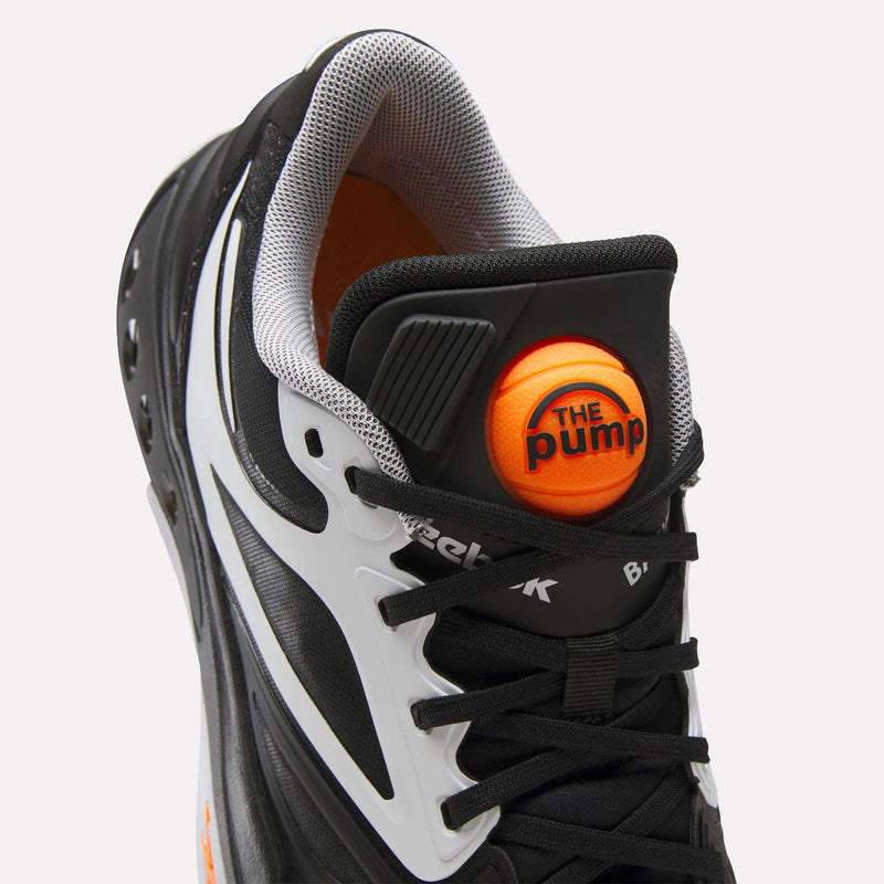 Close-up of a black and white Reebok Engine A Pump shoe featuring an orange spherical The Pump button on the tongue.