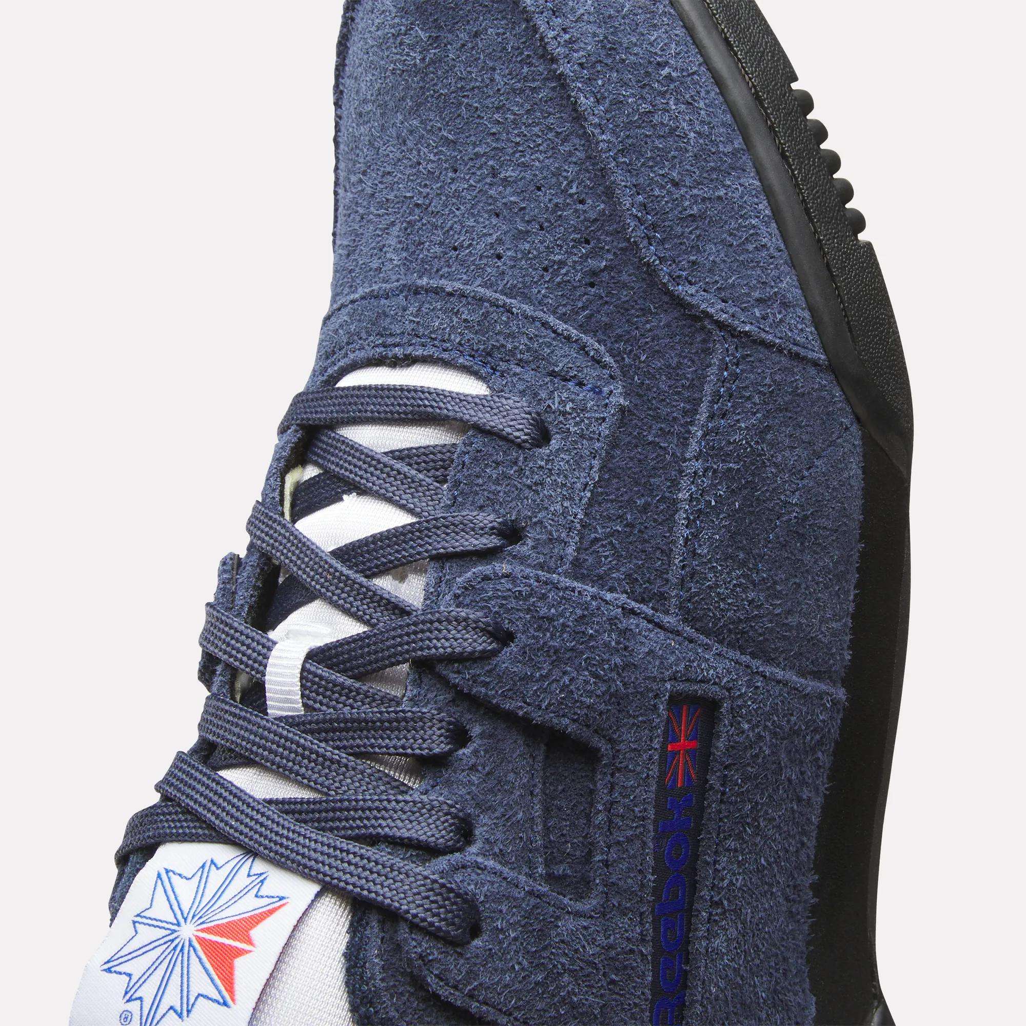 Close-up of Reebok Workout Plus Shoes in navy suede, featuring blue laces, a white tongue with the Reebok logo and Union Jack flag—classic 80s fitness style.