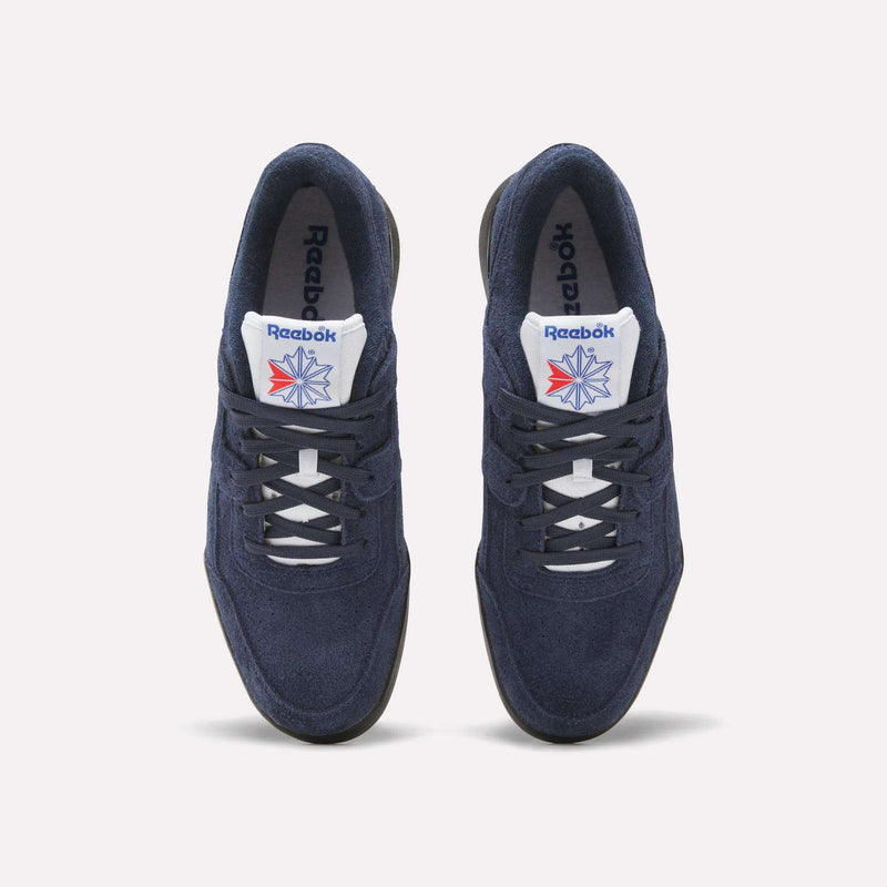 A pair of Reebok Workout Plus Shoes in navy blue with white laces and soles, featuring the Reebok logo and a red-blue star on the white tongue, capture classic '80s style against a light background.
