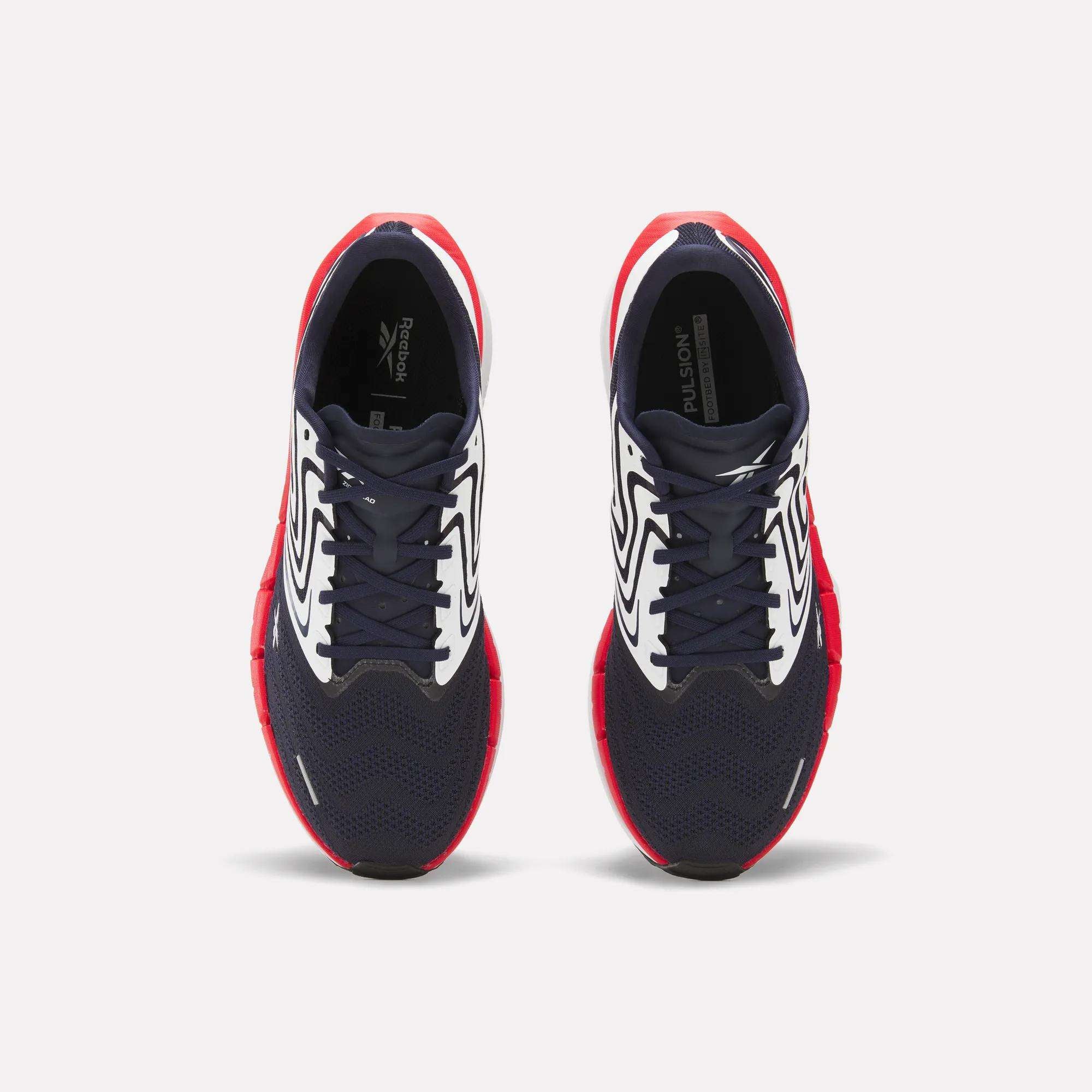 The Reebok Men's FloatZig Tread Running Shoes feature navy blue mesh toes, white patterned sides, and bright red soles—ideal for treadmill workouts. Shown from above against a plain white background.