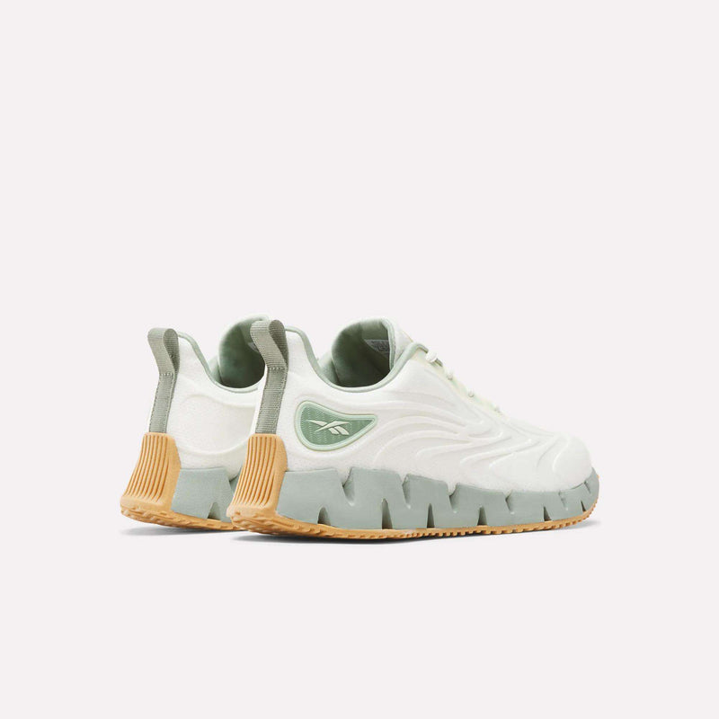 Off-white Reebok Women’s Zig Futaura 1.0 Shoes featuring a sage green heel patch, a zig-zag patterned FuelFoam midsole, and a gum rubber outsole.