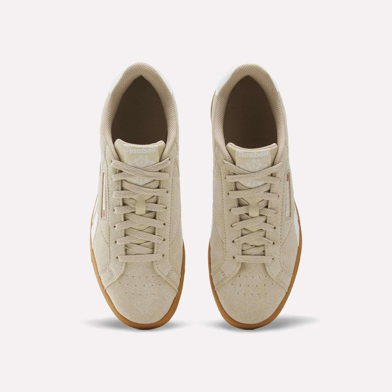 A pair of Reebok Men’s Club C Grounds UK 1.0 shoes in beige with suede accents, white branding labels, and gum soles, shown from above on a plain white background—a subtle homage to classic Reebok style.