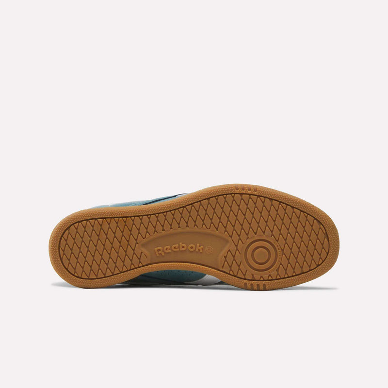 The image shows the sole of the Reebok Men’s Club C Grounds UK 1.0 Shoes, featuring a brown rubber outsole with a herringbone traction pattern and the Reebok logo embossed in the center—a detail that highlights classic Reebok heritage commonly associated with their iconic men’s footwear.