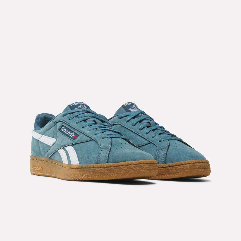 A pair of Men’s Club C Grounds UK 1.0 Shoes by Reebok in teal, featuring classic suede panels, white side stripes, navy accents, and tan rubber soles—these heritage men’s sneakers are displayed on a white background for timeless style.