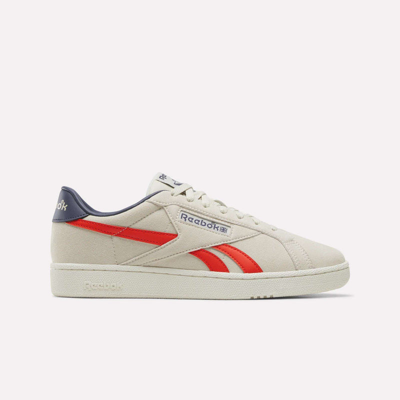 Introducing the Men’s Club C Grounds UK 1.0 Shoes by Reebok, shown here in Linen with Rival Red stripes and a Dark Indigo heel accent. This men’s sneaker features premium suede construction, a classic white sole, and draws inspiration from Reebok’s heritage design. Displayed in a side profile view against a plain light background.