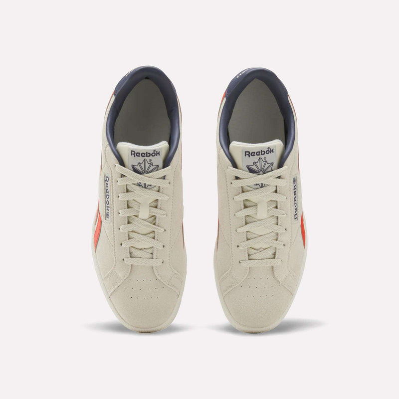 A pair of Reebok Men’s Club C Grounds UK 1.0 Shoes in beige suede with red accents, captured from above to highlight the laces and classic design—reflecting iconic Reebok heritage in men’s footwear.