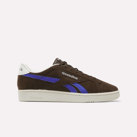 The Reebok Men’s Club C Grounds UK 1.0 Shoes, shown in Espresso suede with Breakout Blue and chalk accents, feature classic side stripes and a white sole—capturing timeless vintage style in men’s footwear.