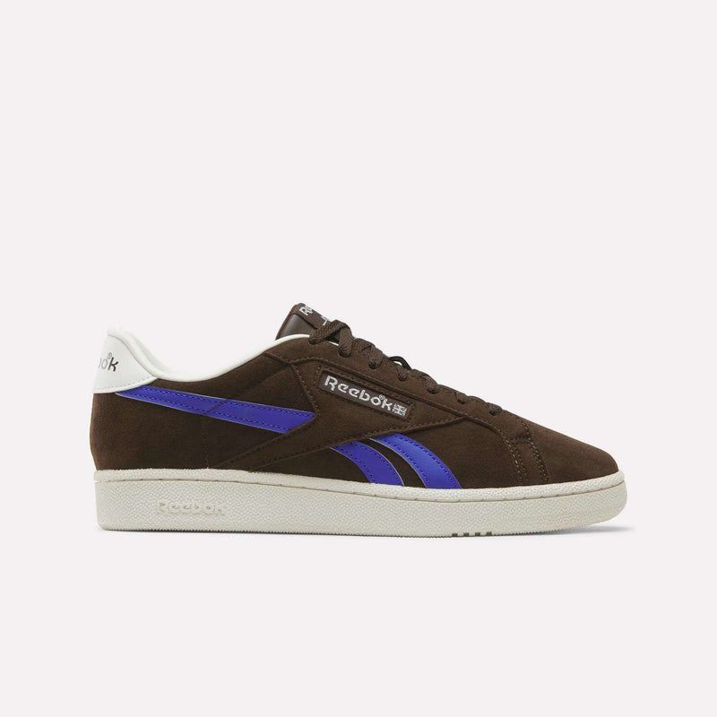The Reebok Men’s Club C Grounds UK 1.0 Shoes, shown in Espresso suede with Breakout Blue and chalk accents, feature classic side stripes and a white sole—capturing timeless vintage style in men’s footwear.