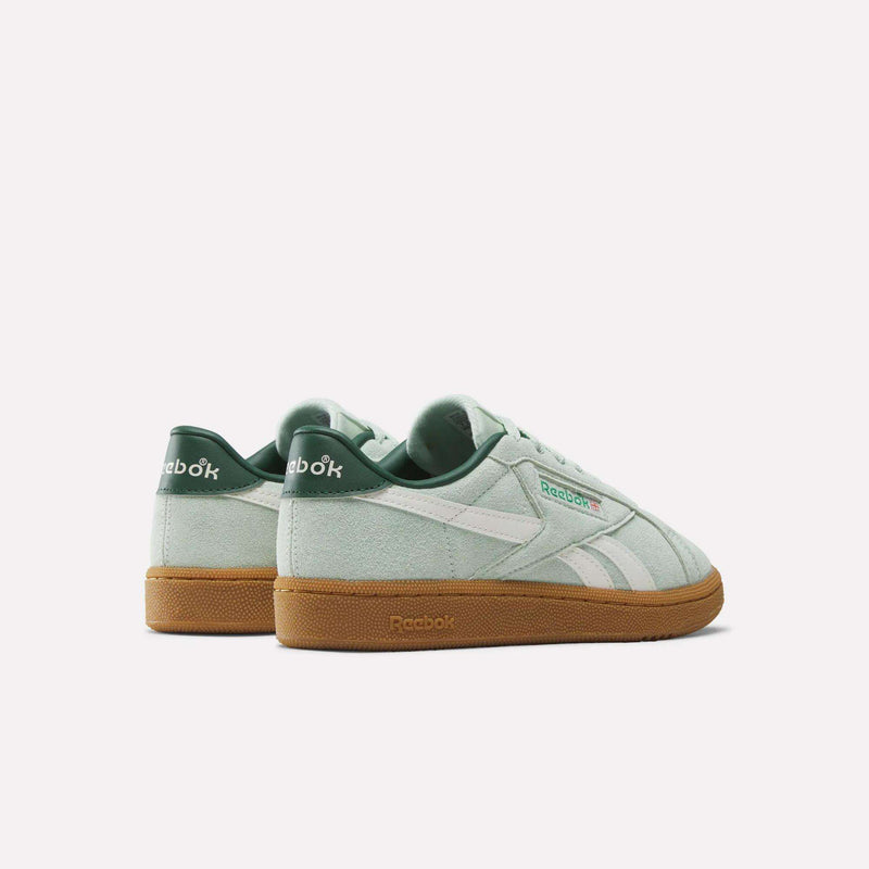 A pair of Reebok Women’s Club C Grounds UK 1.0 Shoes in mint green suede, featuring white stripes and gum soles, is showcased from the back and side to evoke a vintage sneakers vibe against a plain white background.