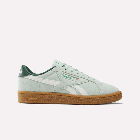 The Reebok Women’s Club C Grounds UK 1.0 Shoes in Green/White/Gum blend vintage-inspired style with modern appeal, featuring a white logo stripe, a dark green heel, and a tan gum sole. This suede sneaker is displayed in side profile against a plain white background.