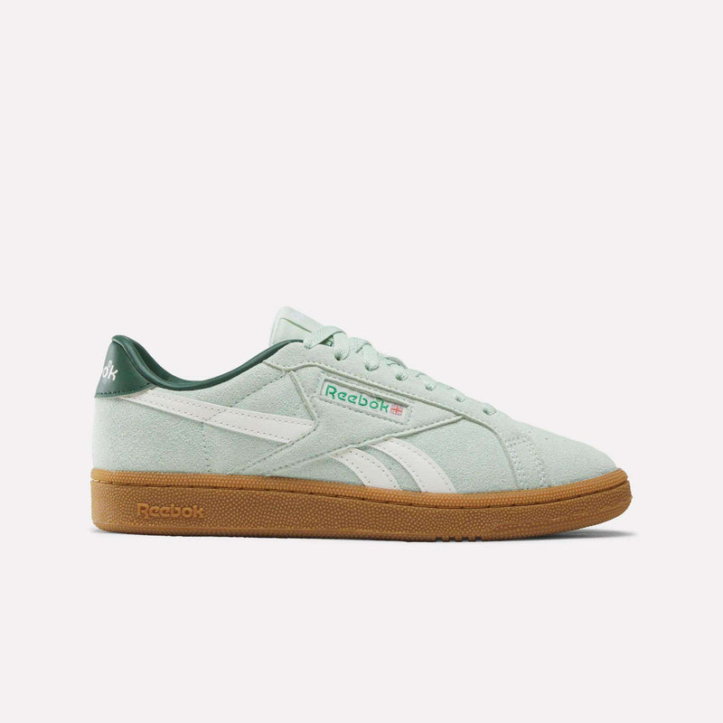 The Reebok Women’s Club C Grounds UK 1.0 Shoes in Green/White/Gum blend vintage-inspired style with modern appeal, featuring a white logo stripe, a dark green heel, and a tan gum sole. This suede sneaker is displayed in side profile against a plain white background.