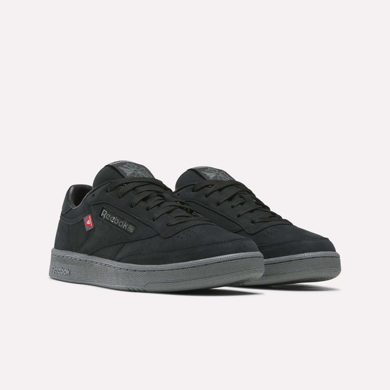 A pair of Reebok Men’s Club C 85 Shoes in black, featuring gray soles, black laces, and red logo accents on the side, displayed on a plain white background.