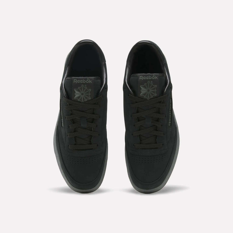 A pair of Men’s Club C 85 Shoes by Reebok in black are displayed from an overhead view, highlighting the laces, perforated toe area, branding on the tongue, and side logo against a light background.