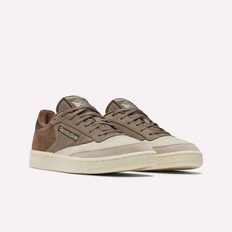 A pair of Men’s Club C 85 Shoes by Reebok in brown and beige hues, crafted with a mix of suede and leather textures, displayed on a plain white background. These retro-inspired sneakers deliver timeless style and comfort, ideal for casual shoe enthusiasts.