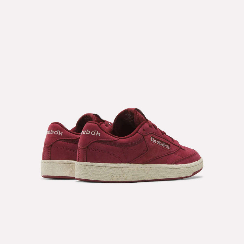 Two maroon Reebok Men’s Club C 85 Shoes with white soles are displayed on a plain light background—one sneaker facing forward and the other positioned at an angle to showcase both the heel and side, emphasizing the classic design and premium nubuck leather upper.