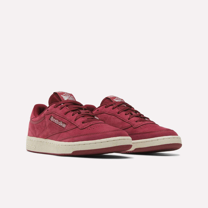 A pair of Men’s Club C 85 Shoes by Reebok in red, featuring off-white soles, displayed against a plain light background. Made with nubuck leather, these tennis sneakers are designed for men and feature the iconic Reebok branding on the side and tongue.