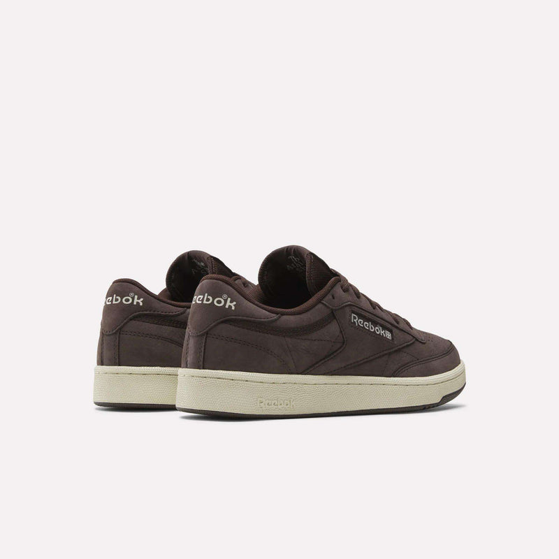 The Reebok Men's Club C 85 Shoes in dark brown nubuck leather with off-white soles are displayed on a plain light background, featuring the Reebok logo on the side and heel.