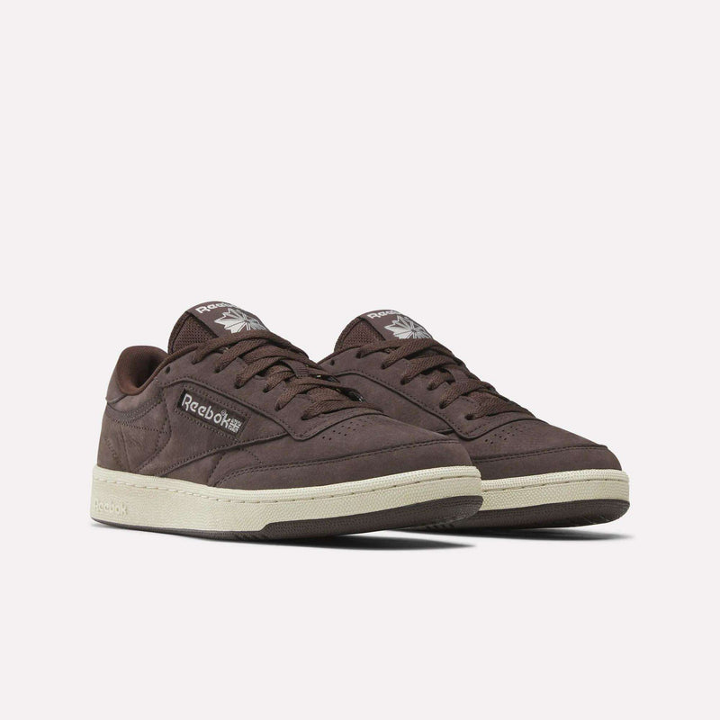 A pair of Men’s Club C 85 Shoes by Reebok in brown with off-white soles is shown on a light background, featuring the Reebok logo on the side and tongue.