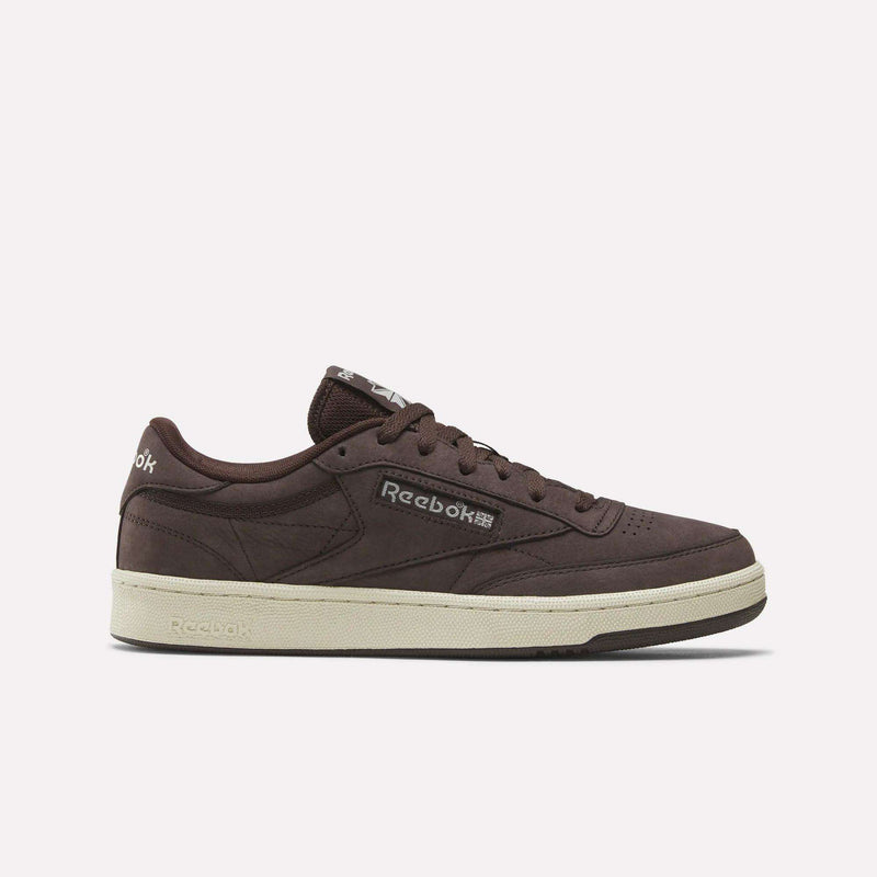 Side view of Reebok Men's Club C 85 Shoes in brown nubuck leather with a cream sole, Reebok logos on the side and tongue, brown laces, and detailed stitching shown against a plain white background.