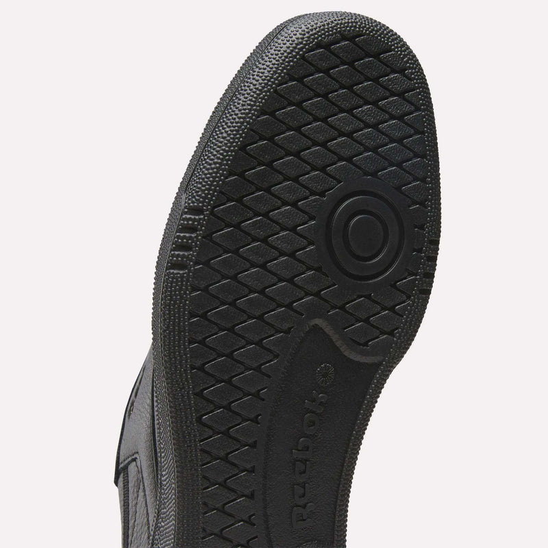 Close-up of the black rubber sole of a Reebok Men’s Club C 85 Shoe featuring a textured, diamond-shaped grip pattern and circular design, with the Reebok logo embossed on the arch area. The upper is crafted from premium garment leather, complementing its timeless silhouette.