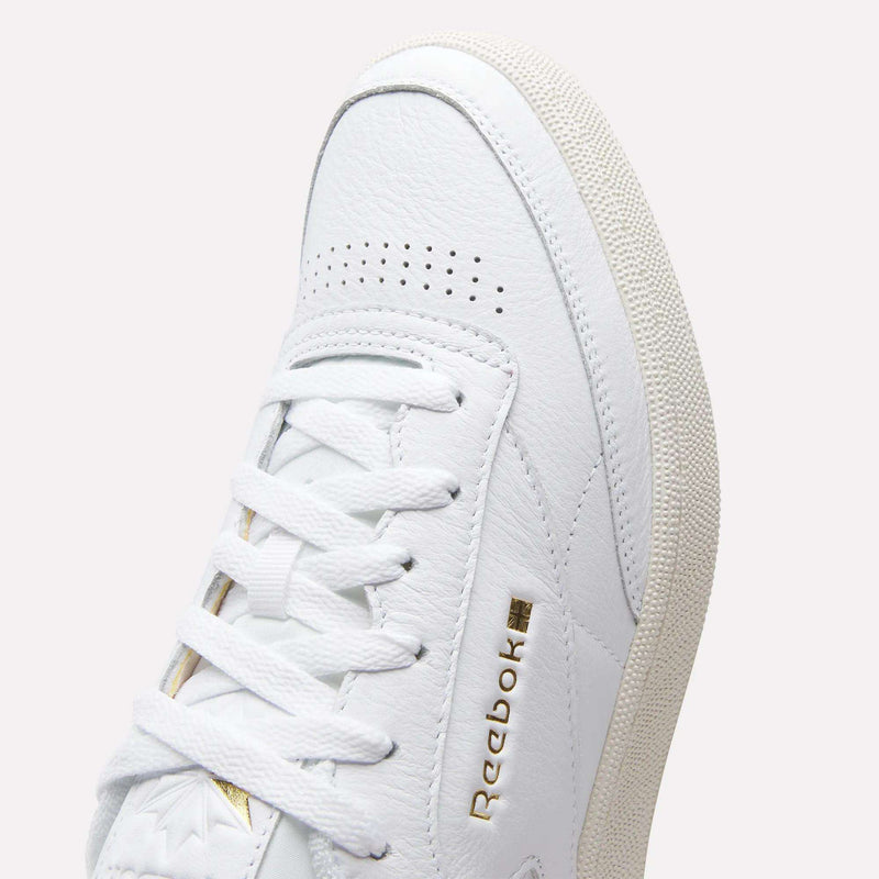 Close-up of Reebok Men's Club C 85 Shoes in white, crafted from premium leather with white laces, textured leather accents, a gold Reebok logo on the side, and a light beige sole with textured grip.