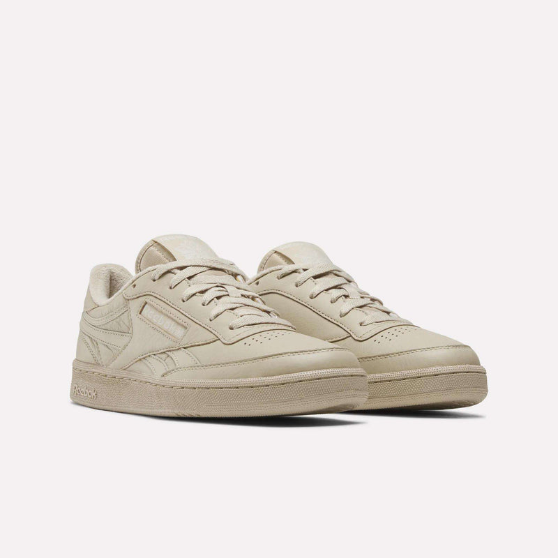 A pair of Reebok Men’s Club C Revenge Shoes in beige, featuring textured soles and subtle stitching details, inspired by classic tennis style, displayed against a plain white background.