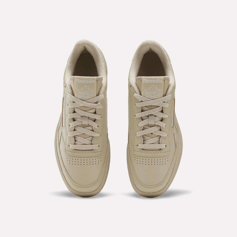 A pair of Men’s Club C Revenge Shoes by Reebok in beige, tennis-inspired and shown from an overhead view with visible laces, perforated toes, and Reebok logos on the tongues, set against a plain white background.