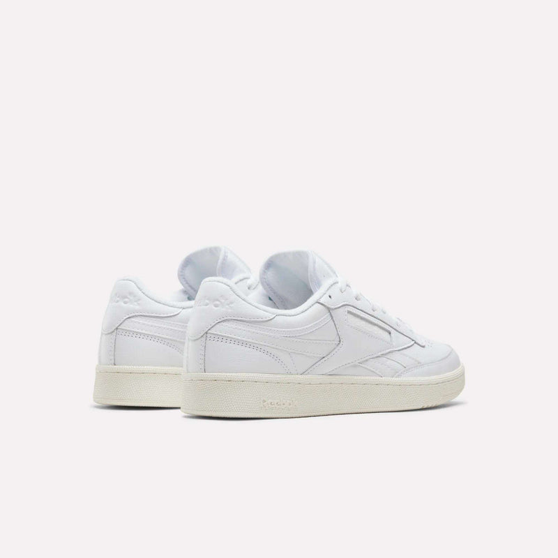 Two Men’s Club C Revenge Shoes by Reebok, featuring white uppers and cream-colored soles, are displayed on a plain white background. The sneakers are positioned to showcase both the back and side views, highlighting their tennis-inspired design.