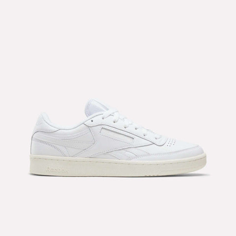 The Reebok Men’s Club C Revenge Shoes in Ftwr White/Chalk are shown in a side profile against a plain light background. This tennis-inspired sneaker features white laces, subtle stitching accents, and a beige rubber sole, blending classic style with modern comfort.
