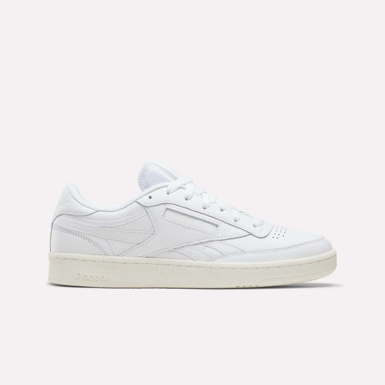 The Reebok Men’s Club C Revenge Shoes in Ftwr White/Chalk are shown in a side profile against a plain light background. This tennis-inspired sneaker features white laces, subtle stitching accents, and a beige rubber sole, blending classic style with modern comfort.