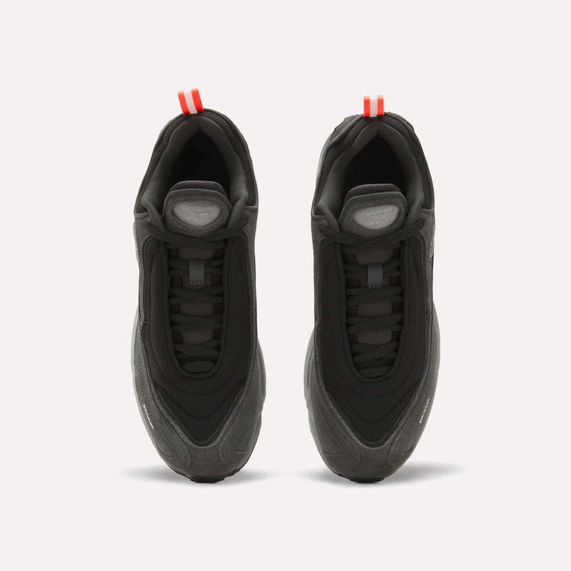 A pair of Men’s Daytona DMX Shoes by Reebok, shown from above in black with thick, air-cushioned soles and striking red pull tabs at the heels—these motorsport-inspired sneakers are set against a clean white background.
